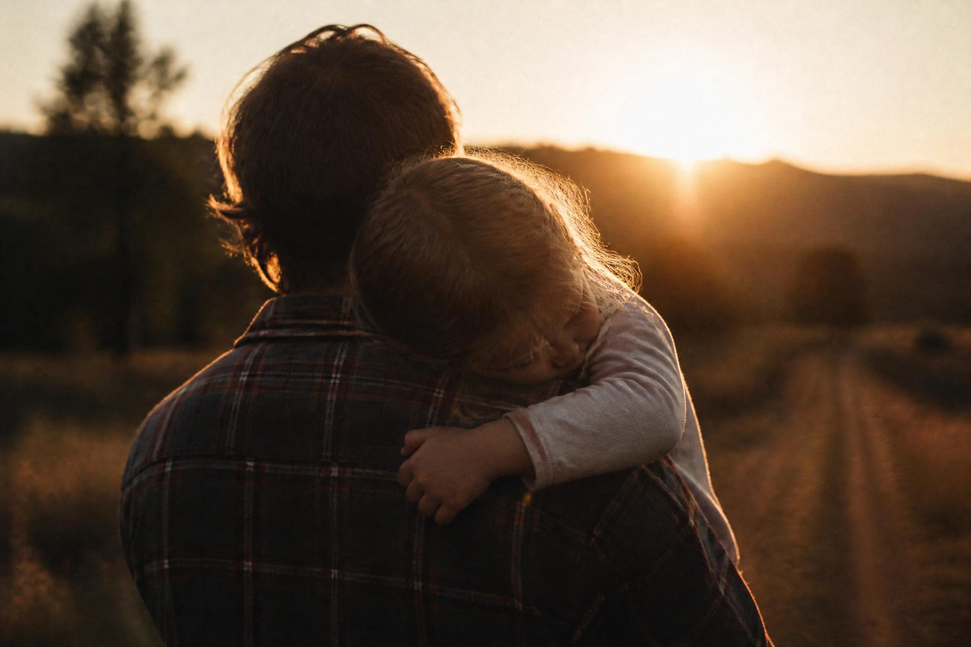 A father carrying his sleeping daughter at sunset