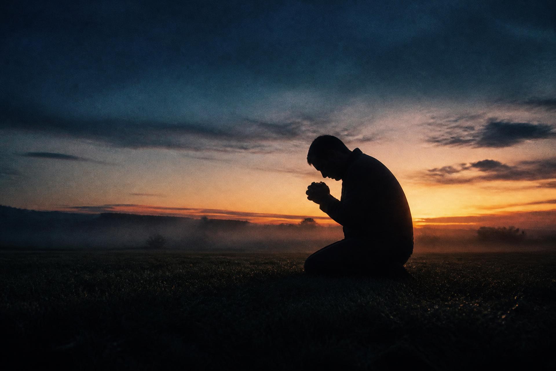 A man kneeling in prayer before sunrise